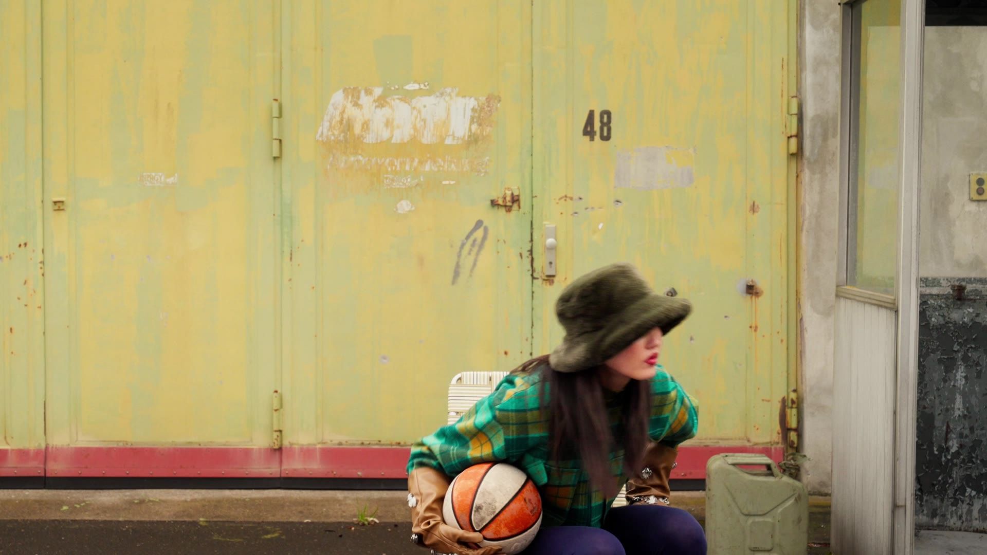 Still from the Blutsgeschwister Fall Winter 26 film: a woman with a basketball in front of a yellow wall