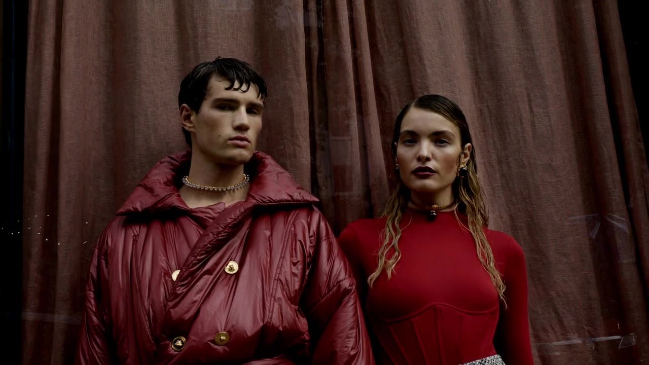 Still from the fashion film »Rich Love« for Latest: two models in red jackets in front of a curtain